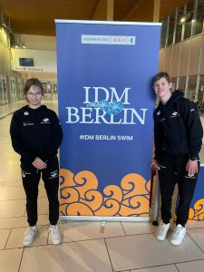 Die Geschwister Emma und Felix vor Plakat des IDM Schwimmen in Berlin